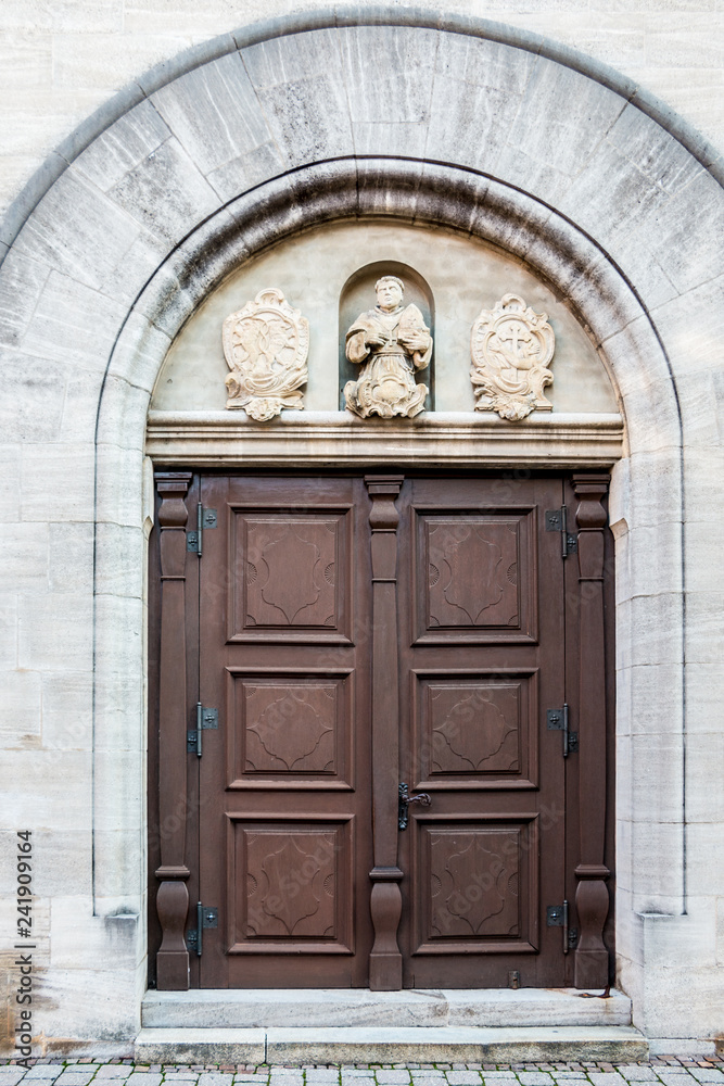 Old door of a historical building with statues and coats of arms made of stone