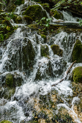 close-up natural landscape with a small waterfall in the forest; landscape in green with bumping water over rocks and moss
