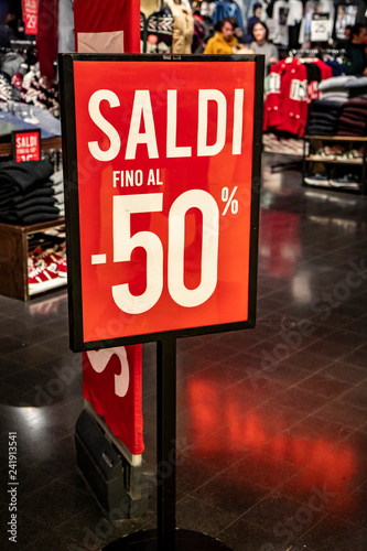 Red sign with the words "Sale up to 50%", in the window of an Italian clothing and fashion store, during the winter sales in January. Clothes and shoes with price tag and discount