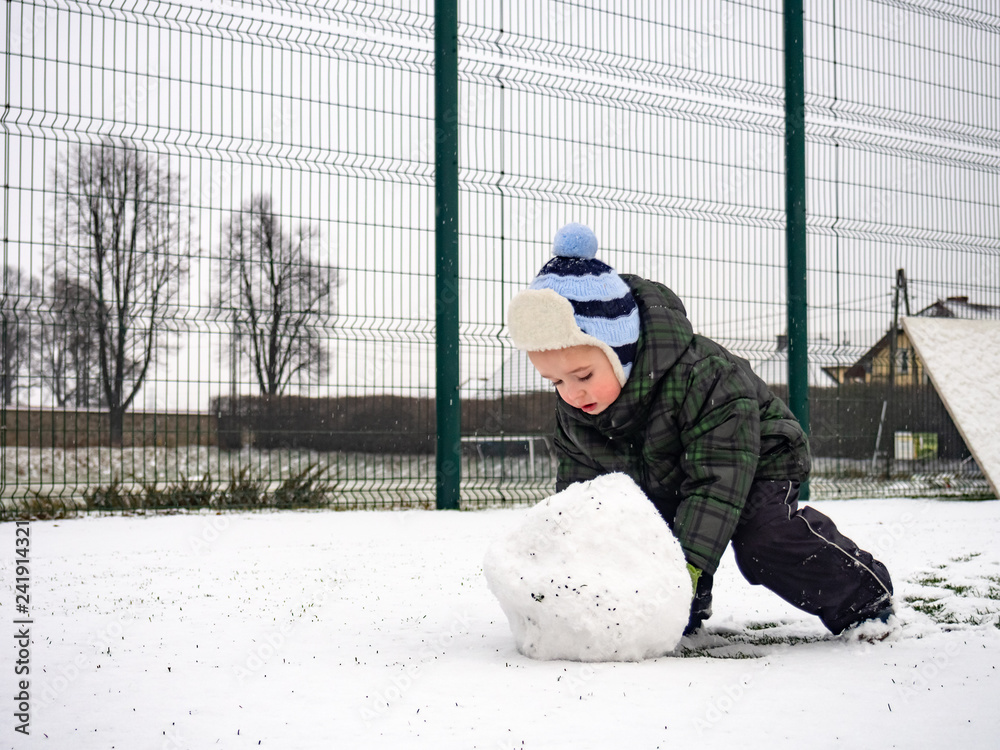 Boy rolling snowball on playground