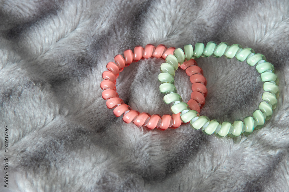 Obraz premium Two pink and Light green blue scrunchy hair tie elastic spring on the silver gray fluffy faux fur blanket background