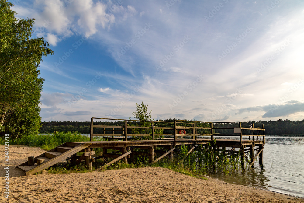 ein See mit Holzsteg umgeben von Wald