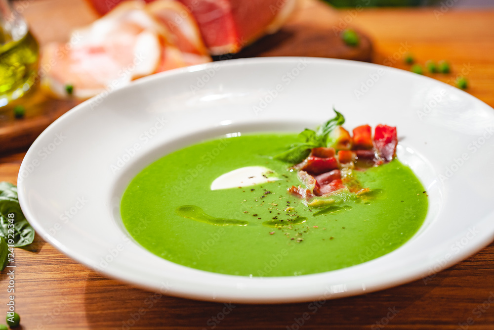 Green pea cream soup with bacon in white plate. Close up Green pea cream soup with bacon in white plate. Close up