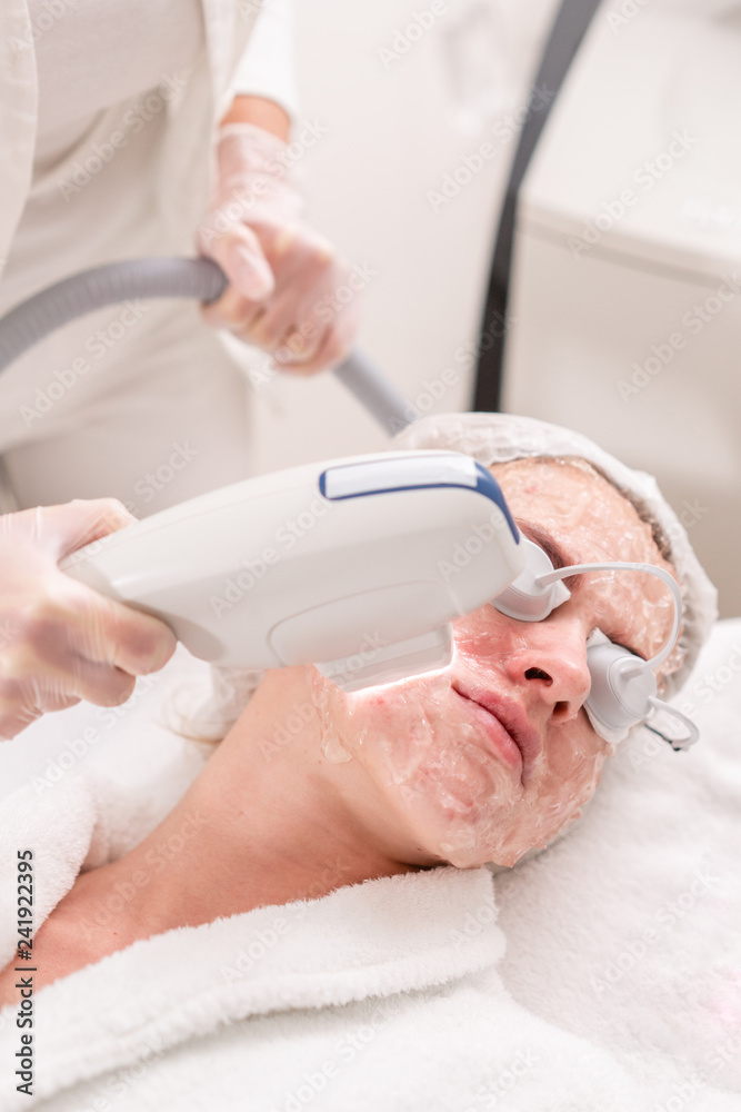 Naklejka premium Anti acne phototherapy with professional equipment. Beautiful woman in beauty salon during photo rejuvenation procedure. Laser face skin treatment at cosmetic clinic. Hardware cosmetology