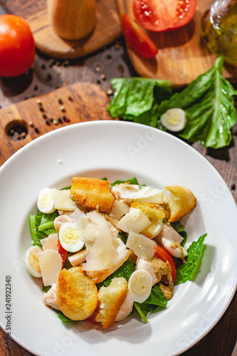 Caesar salad with chicken breast, eggs, croutons, parmesan cheese on white plate. Top view. Close up