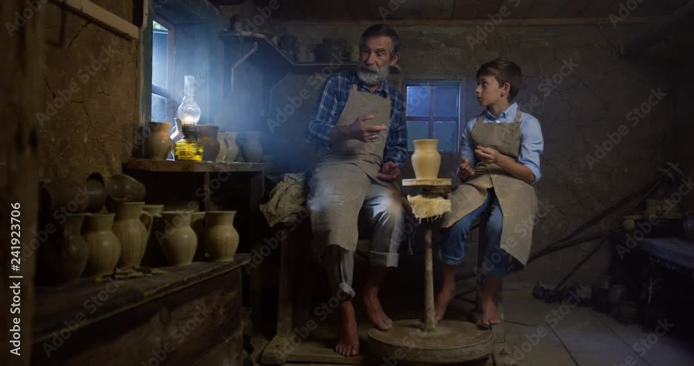 Lesson of the pottery crafting from an old professional potter to the little boy who listening him carefully in the workshop room. Lesson of the pottery crafting from an old professional potter to the little boy who listening him carefully in the workshop room.
