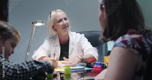 Skilled doctor meeting mother and sick child in hospital office. Female pediatrician, woman with mom, ill young son in medical clinic. Health worker in studio, professional job, medicine. Slow motion