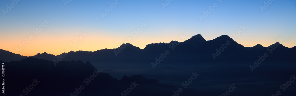 Abstract Image, Mountain Silhouette at sundown - rolling jagged mountain peaks, Orange and Yellow sky gradient fading into Blue Sky. Panoramic Abstract Background Image, Gongga Snow Mountain China