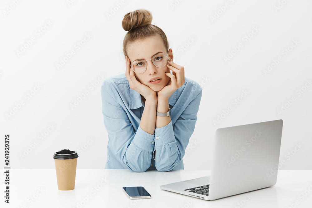 Grl hates her job being bored and sleepy leaning head on table looking indifferent and drained at camera, feeling pressured from load of projects sitting near laptop and smartphone, need more coffee Grl hates her job being bored and sleepy leaning head on table looking indifferent and drained at camera, feeling pressured from load of projects sitting near laptop and smartphone, need more coffee
