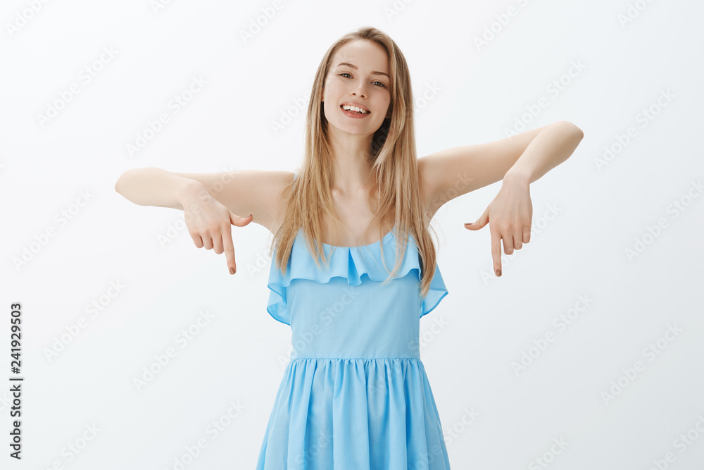 Hey check out my outfit, look down. Portrait of charming good-looking and friendly bright blonde female student on prom hanging out with friend in blue dress pointing downwards as showing cool shoes