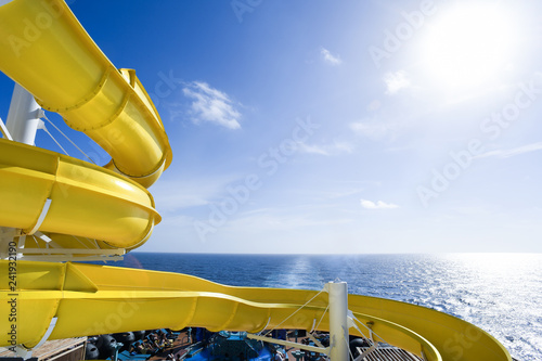 Yellow water slide at the rear of a cruise ship set against a blue sky.
