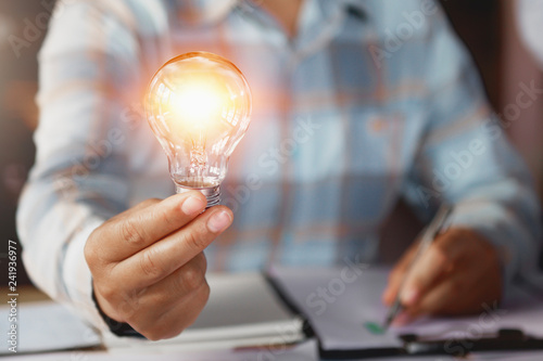 business woman hand holding lightbulb in office. concept saving energy