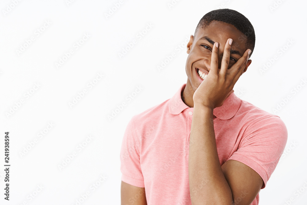 Portrait of charismatic happy good-looking bright african american guy  holding palm on face peeking through fingers, tilting head joyfully and  smiling blushing from sweet comments over gray background Photos | Adobe  Stock