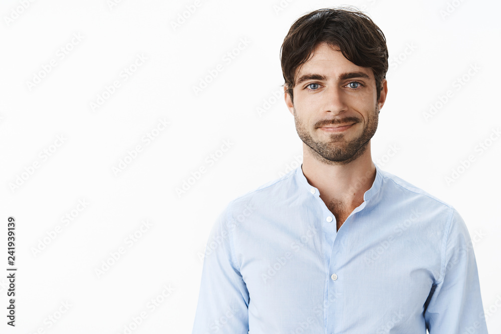 Friendly-looking optimstic and handsome mature and masculine male with blue eyes and bristle smiling joyfully as standing casually in blue shirt against gray background and looking at camera Friendly-looking optimstic and handsome mature and masculine male with blue eyes and bristle smiling joyfully as standing casually in blue shirt against gray background and looking at camera