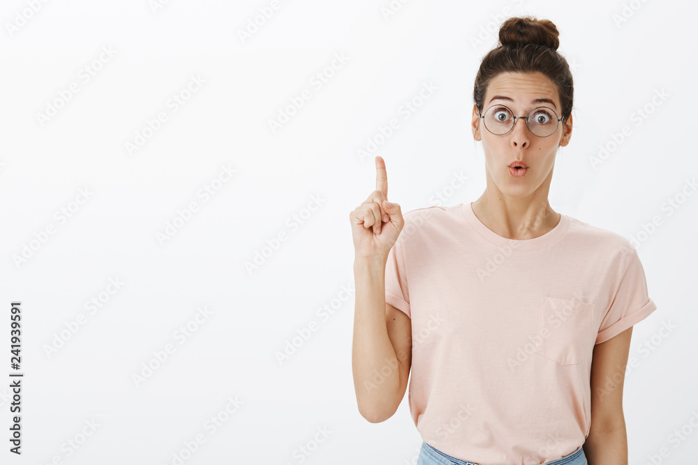 Cute nerdy girl in round glasses folding lips and gasping as raising index finger in eureka gesture having idea, adding suggestion, knowing how solve problem standing stiked with awesome plan Cute nerdy girl in round glasses folding lips and gasping as raising index finger in eureka gesture having idea, adding suggestion, knowing how solve problem standing stiked with awesome plan