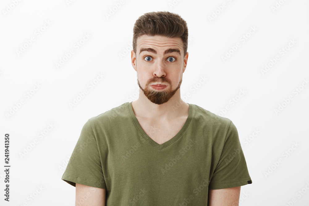 Close-up shot of silly and funny good-looking bearded male in olive t-shirt pouting holding breath looking like balloon raising eyebrows, feeling playful fooling around over white background Close-up shot of silly and funny good-looking bearded male in olive t-shirt pouting holding breath looking like balloon raising eyebrows, feeling playful fooling around over white background