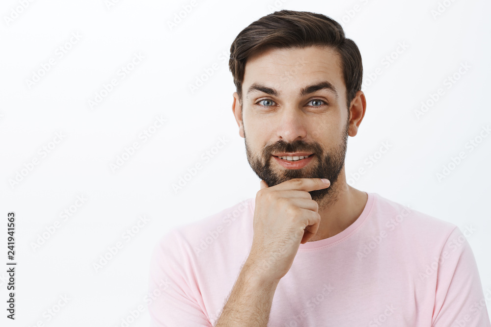 Pleased ambitious and charismatic handsome man rubbing beard smiling with delight at camera having interesting idea thinking having plans for future posing satisfied over gray background Pleased ambitious and charismatic handsome man rubbing beard smiling with delight at camera having interesting idea thinking having plans for future posing satisfied over gray background