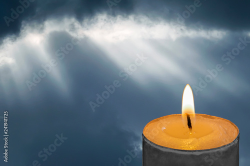 Burning candle on a background of sunlight breaks through the clouds