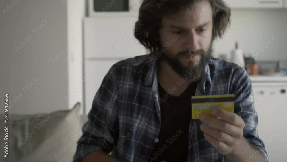 Concentrated bearded young man typing card number on touch screen of modern tablet. Concentrated bearded young man typing card number on touch screen of modern tablet.
