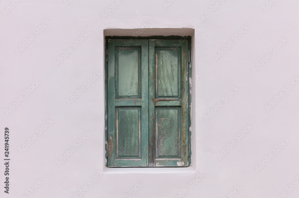 Old fashioned worn window with green wooden shutters, closed, on painted wall background.