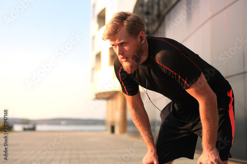 Handsome young man after run resting after jog at the park at sunset or sunrise.