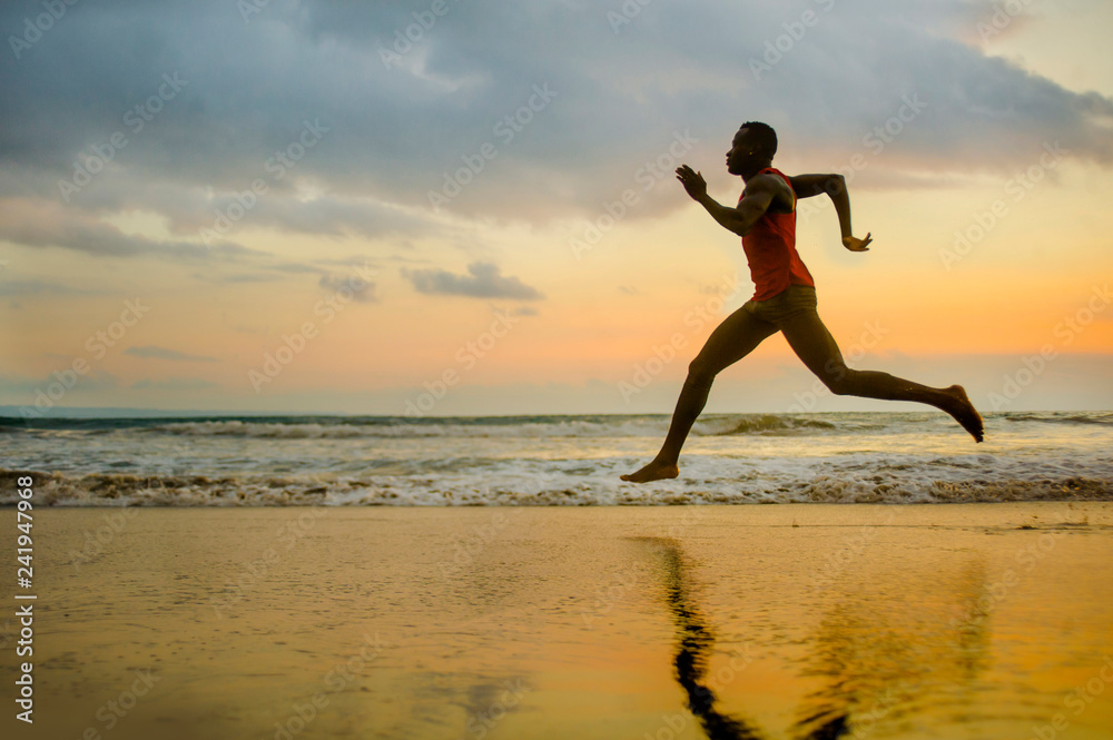 silhouette of young attractive fit athletic and strong black African American man running at sunset beach training hard and sprinting on sea water in runner workout