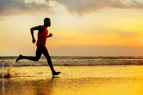 silhouette of young attractive fit athletic and strong black African American man running at sunset beach training hard and sprinting on sea water in runner workout