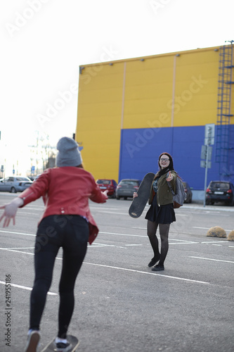 A young hipster girl is riding a skateboard. Girls girlfriends for a walk in the city with a skateboard. Spring sports on the street with a skateboard.