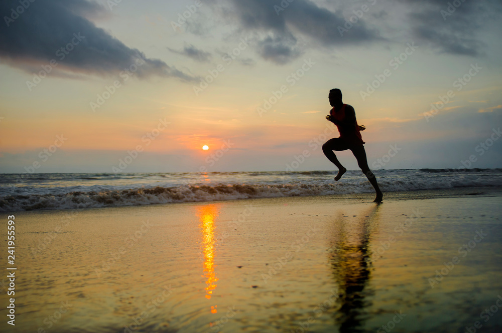 silhouette of young attractive fit athletic and strong black afro American man running at sunset beach training hard and sprinting on sea water runner workout