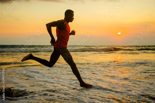 silhouette of young attractive fit athletic and strong black African American man running at sunset beach training hard and sprinting on sea water runner workout