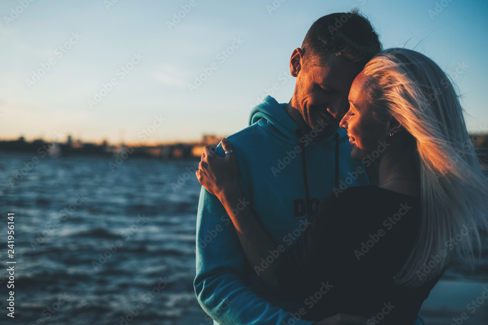 Silhouette of couple in love on the pier, sunset time, water bac