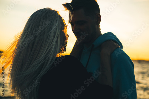 Silhouette of couple in love on the pier, sunset time, water bac
