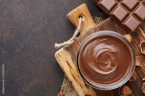 Chocolate spread or nougat cream with hazelnuts in glass jar on brown textured countertop, copy space