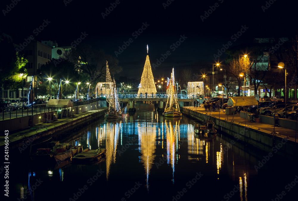 View of the Christmas Tree on a bridge at night, with reflections. Long exposure picture in Riccione, Emilia Romagna, Italy.