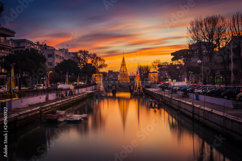 View of the Christmas Tree on a bridge at sunset, with orange clouds. Long exposure picture in Riccione, Emilia Romagna, Italy.