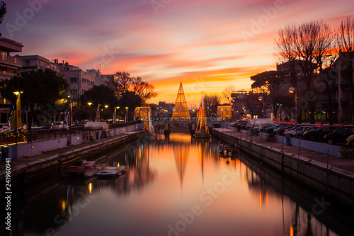 View of the Christmas Tree on a bridge at sunset, with orange clouds. Long exposure picture in Riccione, Emilia Romagna, Italy.