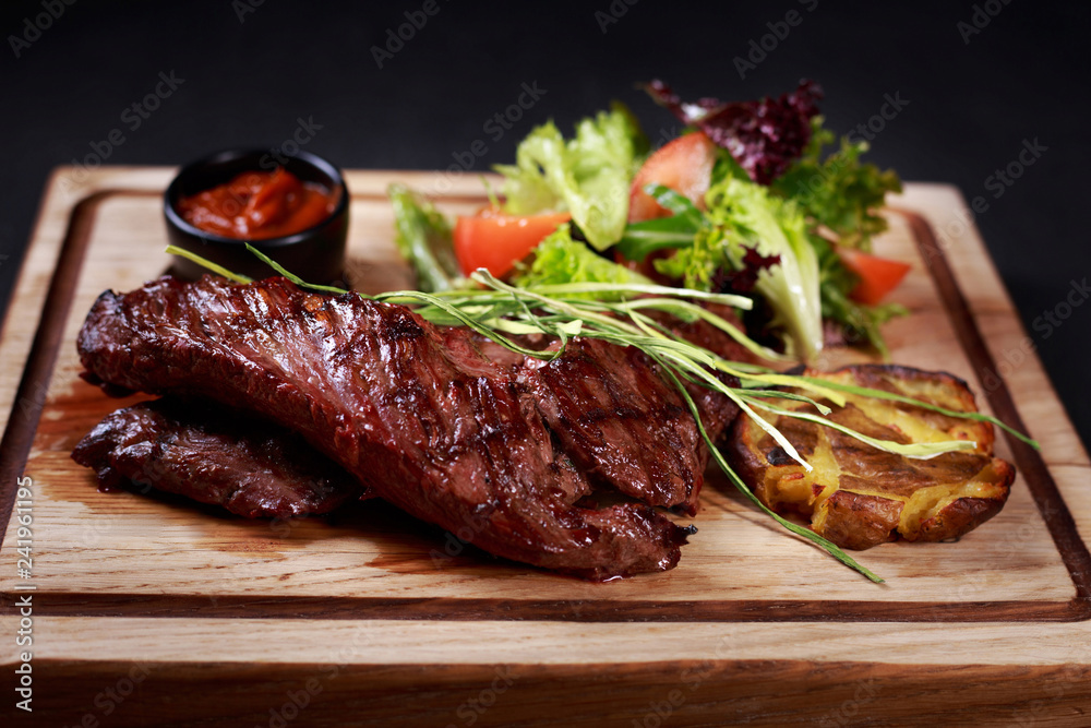 grill and barbeque, meat restaurant menu, juicy medium rare skirt steak served with vegetable salad and potatoes on board, traditional american cuisine grill and barbeque, meat restaurant menu, juicy medium rare skirt steak served with vegetable salad and potatoes on board, traditional american cuisine