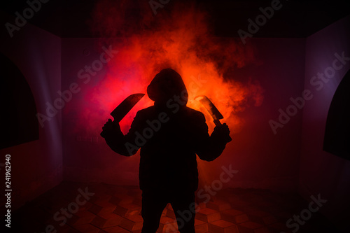 A dangerous hooded man standing in the dark and holding a knife. Face can not be seen. Committing a crime concept. Selective focus