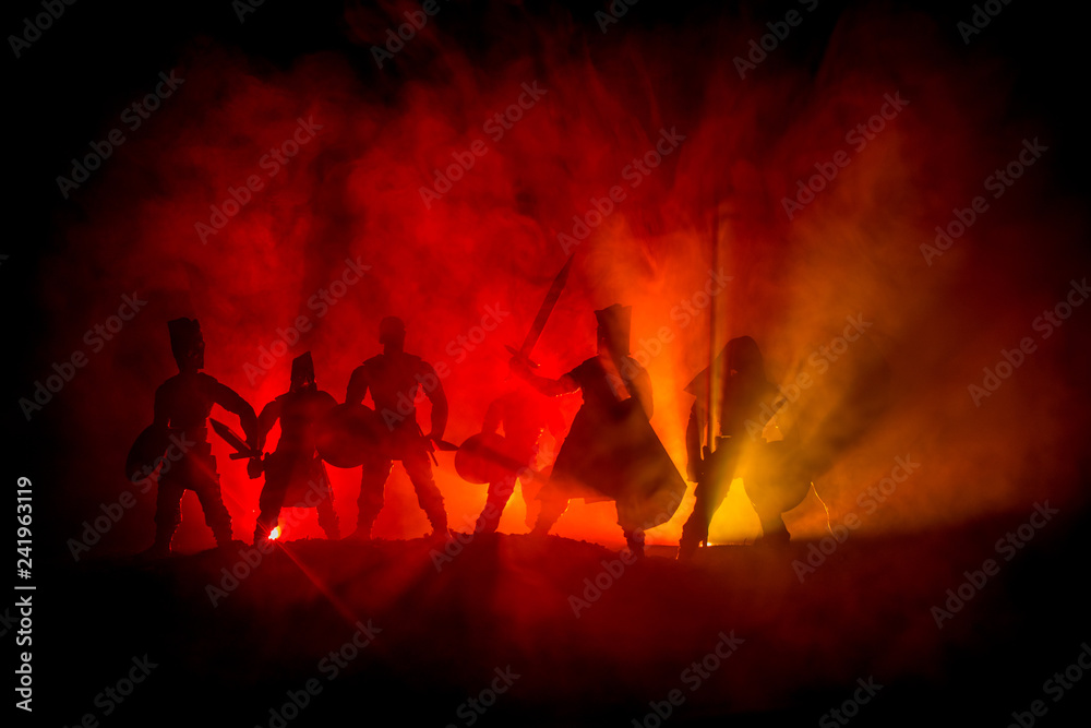 Fototapeta premium Medieval battle scene. Silhouettes of figures as separate objects, fight between warriors on dark toned foggy background. Night scene.