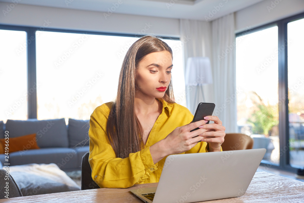 Young woman text messaging while sitting behind her laptop and working from home Young woman text messaging while sitting behind her laptop and working from home