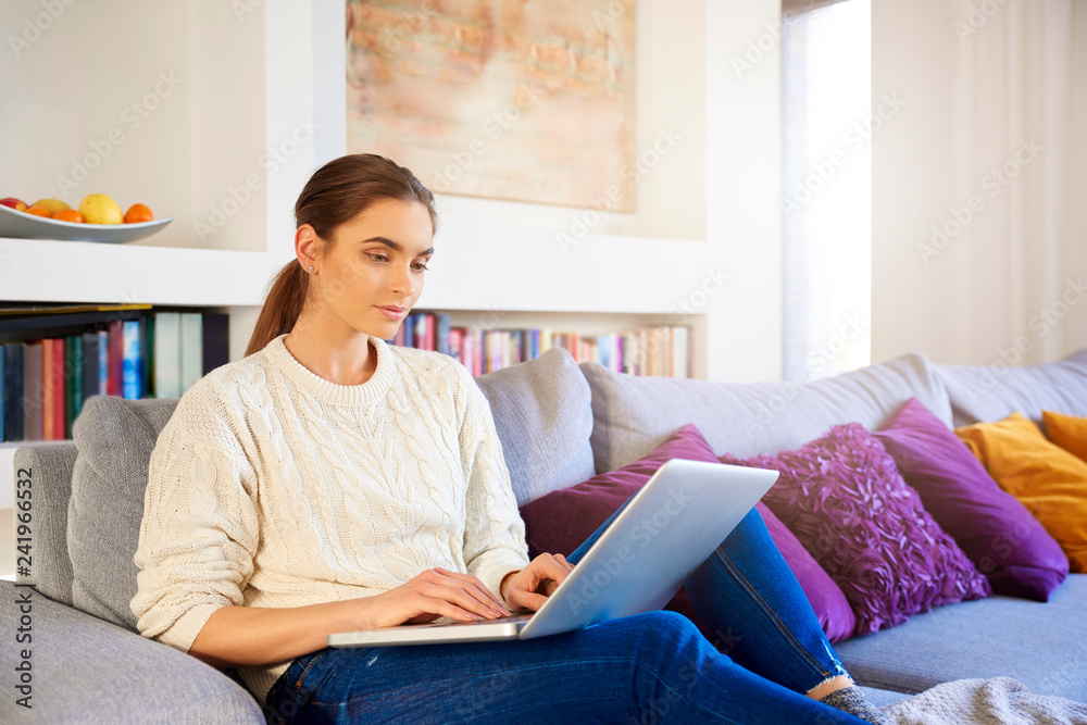 Beautiful young woman with her laptop sitting on couch Beautiful young woman with her laptop sitting on couch