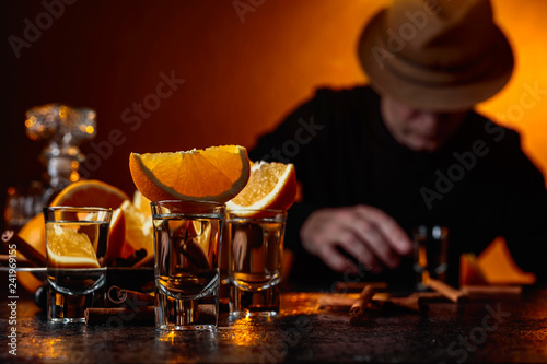 Glasses of tequila with orange and cinnamon sticks on a table in bar.