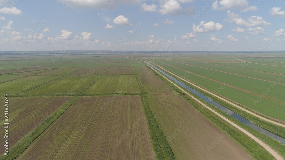 Aerial view of agricultural cultivated fields with irrigational channel. Agricultural landscape rows. Irrigated farmland. Countryside with fields of crops.