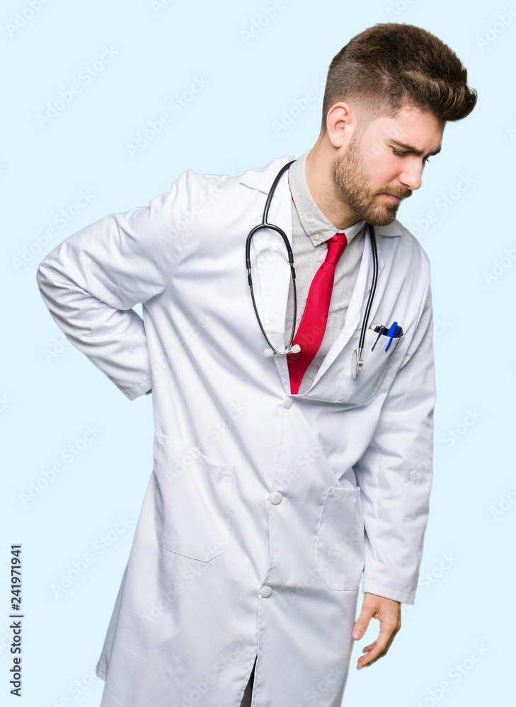 Young handsome doctor man wearing medical coat Suffering of backache, touching back with hand, muscular pain Young handsome doctor man wearing medical coat Suffering of backache, touching back with hand, muscular pain