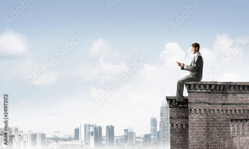 Man on roof edge send message with smartphone and cityscape at background