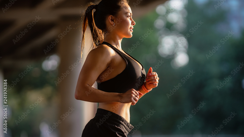 Portrait Shot of a Beautiful Busty Fitness Girl in Black Athletic Top and  Shorts is Energetically Running in the Street. She is Jogging in an Urban  Environment Under a Bridge. Stock Photo