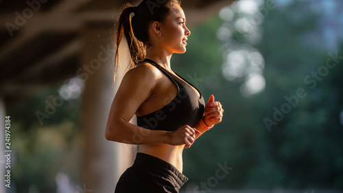 Portrait Shot of a Beautiful Busty Fitness Girl in Black Athletic Top and Shorts is Energetically Running in the Street. She is Jogging in an Urban Environment Under a Bridge.