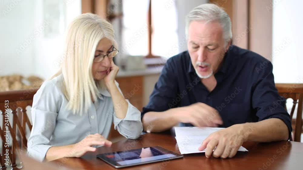 Senior couple working out their bills at home in the kitchen Senior couple working out their bills at home in the kitchen