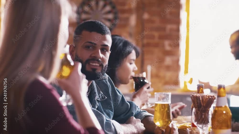 Young Arabian man talking with Caucasian girl near bar counter inside pub