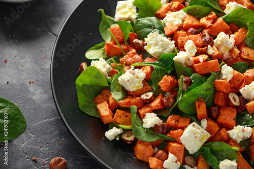 Healthy roasted sweet potato salad with spinach, feta cheese, hazelnut nuts in black plate